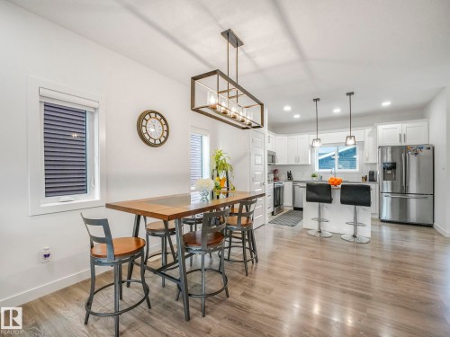 Expansive wood-finish flooring throughout, complemented by a modern linear chandelier and recessed lighting - 3807 Weidle Crescent Sw, Edmonton, AB 
