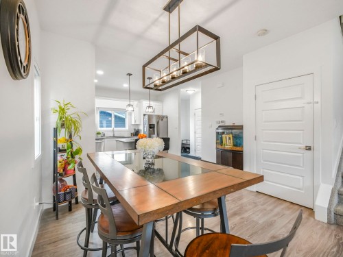 Wood-finish flooring, white paneled door, and a modern rectangular chandelier - 3807 Weidle Crescent Sw, Edmonton, AB 