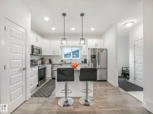 Modern kitchen featuring stainless steel appliances, white cabinetry, a central island with pendant lighting, and wood-finish flooring - 3807 Weidle Crescent Sw, Edmonton, AB 