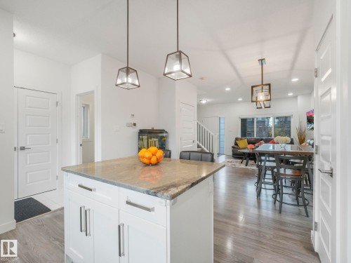 Open-concept living space featuring wood-finish flooring, recessed lighting, and a kitchen island with stone countertops - 3807 Weidle Crescent Sw, Edmonton, AB 