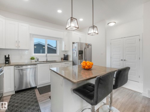 Kitchen featuring white shaker cabinetry, stainless steel appliances, a center island with countertop seating, and wood-finish flooring - 3807 Weidle Crescent Sw, Edmonton, AB 