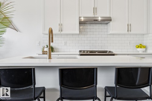 White cabinetry with brushed nickel hardware, stainless steel range hood, subway tile backsplash, and a gold-finish gooseneck faucet - 22434 99A Avenue Nw, Edmonton, AB 
