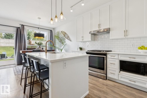 Kitchen featuring a central island with countertop seating, white cabinetry, stainless steel appliances, a subway tile backsplash, and wood-finish flooring - 22434 99A Avenue Nw, Edmonton, AB 