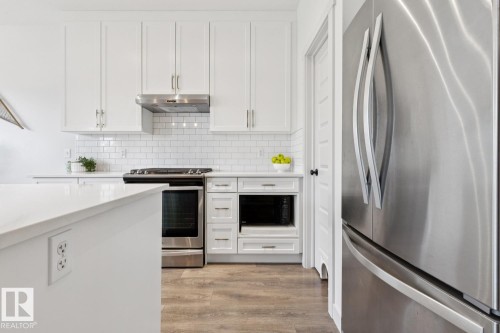 White shaker cabinetry with gold-finish hardware, stainless steel appliances, subway tile backsplash, white countertop, and wood-finish flooring - 22434 99A Avenue Nw, Edmonton, AB 