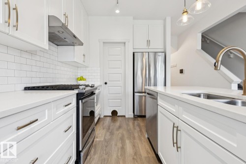 White shaker cabinetry, stainless steel appliances, subway tile backsplash, light-toned wood-finish flooring, and pendant lighting - 22434 99A Avenue Nw, Edmonton, AB 