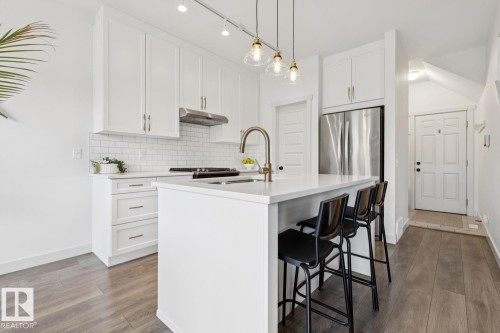Modern kitchen featuring white cabinetry, subway tile backsplash, stainless steel appliances, and a central island with counter seating - 22434 99A Avenue Nw, Edmonton, AB 