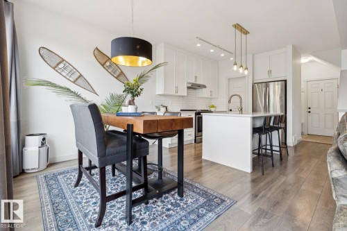 Hardwood-style flooring, white kitchen cabinetry, stainless steel appliances, kitchen island with seating, pendant lighting - 22434 99A Avenue Nw, Edmonton, AB 
