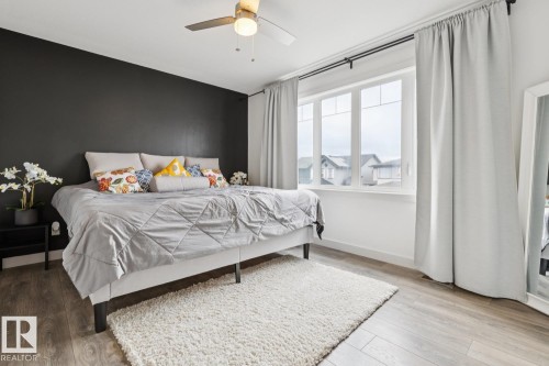 Expansive window with white trim, wood-finish flooring, a ceiling fan with integrated lighting, and a dark accent wall - 22434 99A Avenue Nw, Edmonton, AB 