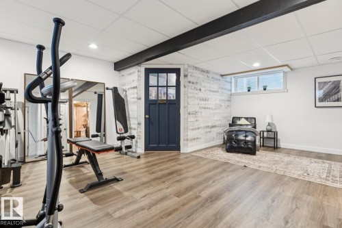 Spacious room featuring wood-finish flooring, a textured accent wall, recessed lighting, and a window with blinds - 22434 99A Avenue Nw, Edmonton, AB 