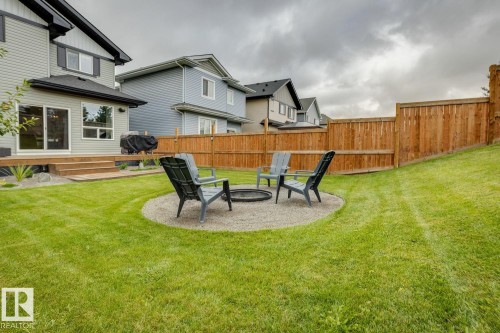 Expansive backyard featuring a manicured lawn, wood privacy fencing, and a gravel fire pit area - 22434 99A Avenue Nw, Edmonton, AB 