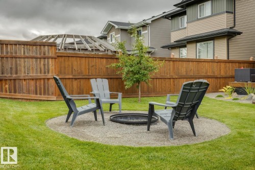 Expansive backyard featuring a manicured lawn, a gravel patio with a built-in fire pit, and a tall wood privacy fence - 22434 99A Avenue Nw, Edmonton, AB 