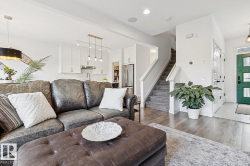 White kitchen cabinetry with stainless steel appliances, wood-finish flooring, and a carpeted staircase - 22434 99A Avenue Nw, Edmonton, AB 