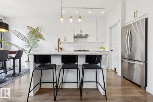 Modern kitchen featuring white cabinetry, subway tile backsplash, a center island with countertop seating, stainless steel appliances, and wood-finish flooring - 22434 99A Avenue Nw, Edmonton, AB 
