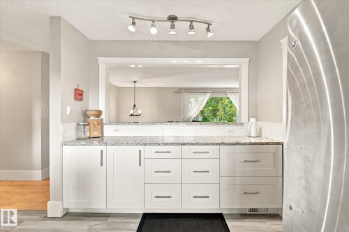 White shaker-style cabinetry, light-toned stone countertops, white tile backsplash, and a pass-through window with white trim - 3 Akins Drive, St. Albert, AB 