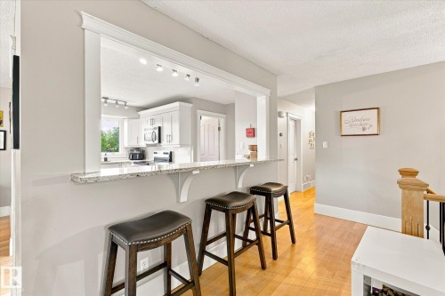 Pass-through kitchen with white cabinetry, stainless steel appliances, recessed lighting, and a granite-finish breakfast bar - 3 Akins Drive, St. Albert, AB 