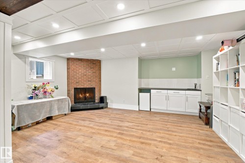 Wood-finish flooring, brick fireplace with a black tile hearth, white paneled ceiling, recessed lighting, and a built-in wet bar with white cabinetry - 3 Akins Drive, St. Albert, AB 