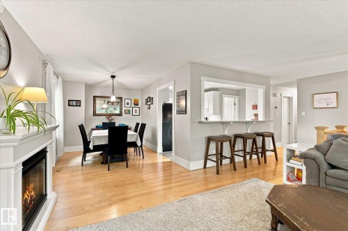 Wood-finish flooring throughout, a built-in fireplace with a white mantel, and a dining area with a contemporary pendant light fixture - 3 Akins Drive, St. Albert, AB 