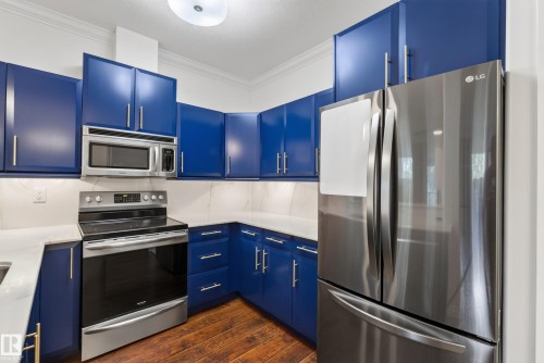 Blue cabinetry, stainless steel appliances, white countertops, built-in microwave, and wood-finish flooring - #210 10121 80 Av Nw, Edmonton, AB 