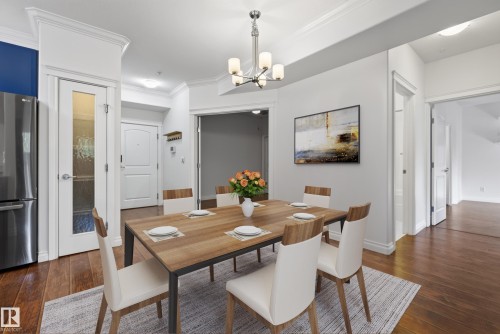 Hardwood-finish flooring, crown molding, brushed nickel chandelier, and a stainless steel refrigerator - #210 10121 80 Av Nw, Edmonton, AB 