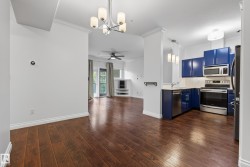 Rich wood-finish flooring throughout, bright white walls, modern chandelier, blue cabinetry, and stainless steel appliances - 