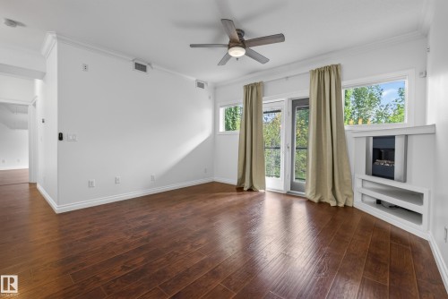 Wood-finish flooring, crown molding, built-in fireplace, ceiling fan, and a glass-paned door leading to a balcony - #210 10121 80 Av Nw, Edmonton, AB 