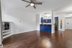 Dark wood-finish flooring with a ceiling fan, a built-in fireplace with shelving, and a kitchen featuring blue cabinetry and stainless steel appliances - 