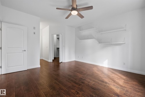 Wood-finish flooring throughout, bright white walls, modern ceiling fan, white interior door, and floating wall shelves - #210 10121 80 Av Nw, Edmonton, AB 