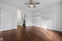Wood-finish flooring throughout, bright white walls, modern ceiling fan, white interior door, and floating wall shelves - 