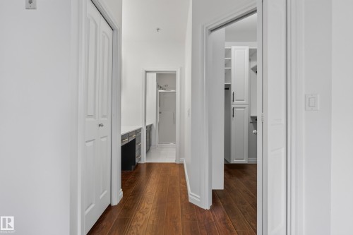 Hardwood-finish flooring extending through the hallway, white bi-fold closet doors, built-in vanity with countertop, and an additional built-in storage unit - #210 10121 80 Av Nw, Edmonton, AB 
