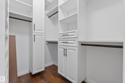 Custom built-in closet system featuring white cabinetry, multiple storage shelves, hanging rods, and integrated drawers with dark hardware - 