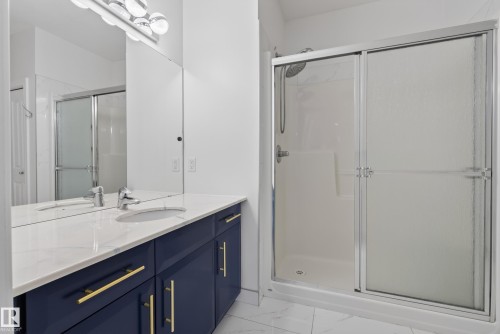 Contemporary vanity with a white countertop and navy cabinetry, single undermount sink, wall-mounted mirror, and overhead lighting - #210 10121 80 Av Nw, Edmonton, AB 