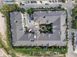 Multi-unit building featuring a central courtyard with landscaping, gabled rooflines, and surrounding paved areas - 