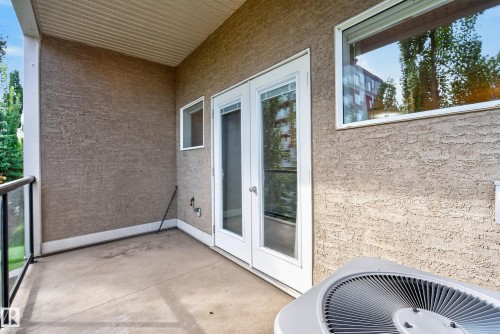 Concrete balcony featuring a stucco exterior, white framed glass paneled double doors, a white framed window, and a glass panel railing - #210 10121 80 Av Nw, Edmonton, AB 