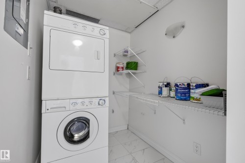 Stackable washer and dryer, white tiled flooring, wall-mounted shelving, and a semi-flush mount light fixture - #210 10121 80 Av Nw, Edmonton, AB 