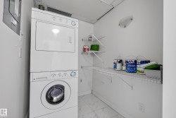 Stackable washer and dryer, white tiled flooring, wall-mounted shelving, and a semi-flush mount light fixture - 
