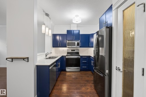Kitchen featuring wood-finish flooring, blue cabinetry, stainless steel appliances, and white countertops - #210 10121 80 Av Nw, Edmonton, AB 