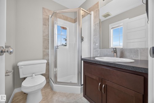 Corner glass shower enclosure with a window, single vanity with dark wood-finish cabinetry, oval undermount sink, and tiled flooring - 483 Watt Boulevard Sw, Edmonton, AB 