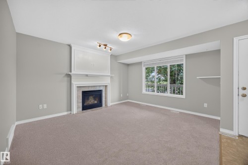 Recessed fireplace with tile surround and decorative mantel, large window with ample natural light, soft carpet flooring, and a built-in wall shelf - 483 Watt Boulevard Sw, Edmonton, AB 