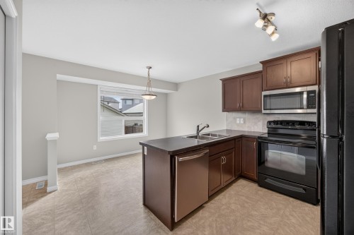 Kitchen featuring wood-finish cabinetry, stainless steel microwave, black appliances, and a dual basin sink - 483 Watt Boulevard Sw, Edmonton, AB 