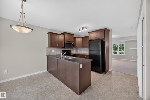 Kitchen featuring rich wood-finish cabinetry, black appliances, a tiled backsplash, and a corner sink - 483 Watt Boulevard Sw, Edmonton, AB 