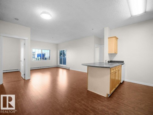 Wood-finish flooring throughout, featuring a kitchen island with sink, upper and lower cabinetry, and a sliding glass door to a balcony - #116 16807 100 Av Nw, Edmonton, AB 