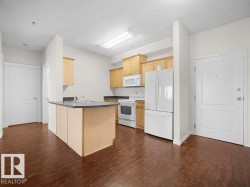 Kitchen featuring wood-finish flooring, wood cabinetry, stone-finish countertops, white appliances, and a central island with an integrated sink - 