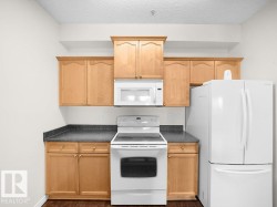 Kitchen featuring wood-finish cabinetry, dark countertops, and a full suite of white appliances including a refrigerator, range, and built-in microwave - 