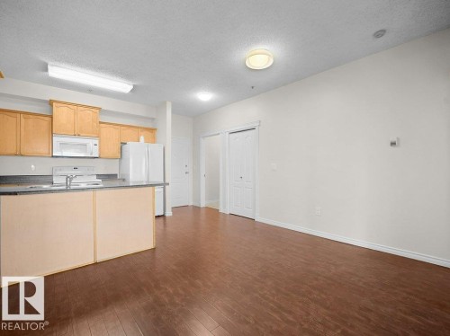 Kitchen with wood-finish cabinetry, stainless steel appliances, and a breakfast bar - #116 16807 100 Av Nw, Edmonton, AB 
