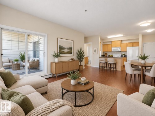 Open-concept living space featuring wood-finish flooring, a sliding glass door to an outdoor patio, a kitchen with wood cabinetry and white appliances, and an integrated dining area - #116 16807 100 Av Nw, Edmonton, AB 