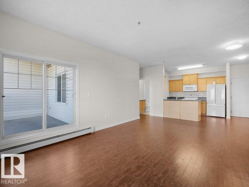 Wood-finish flooring throughout, sliding glass door with balcony access, kitchen with warm wood-finish cabinetry, built-in microwave, and breakfast bar - #116 16807 100 Av Nw, Edmonton, AB 