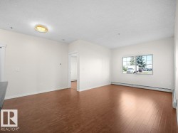 Expansive living area featuring wood-finish flooring, neutral wall tones, a large window, and white trim throughout - 