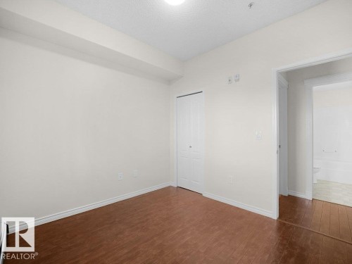 Second bedroom- Wood-finish flooring, white walls, and a built-in closet with bi-fold doors - #116 16807 100 Av Nw, Edmonton, AB 