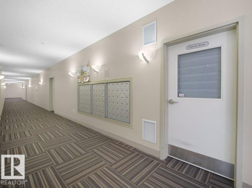 Corridor featuring patterned carpet flooring, wall-mounted light fixtures, and a centralized mailbox system - #116 16807 100 Av Nw, Edmonton, AB 