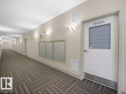 Corridor featuring patterned carpet flooring, wall-mounted light fixtures, and a centralized mailbox system - 